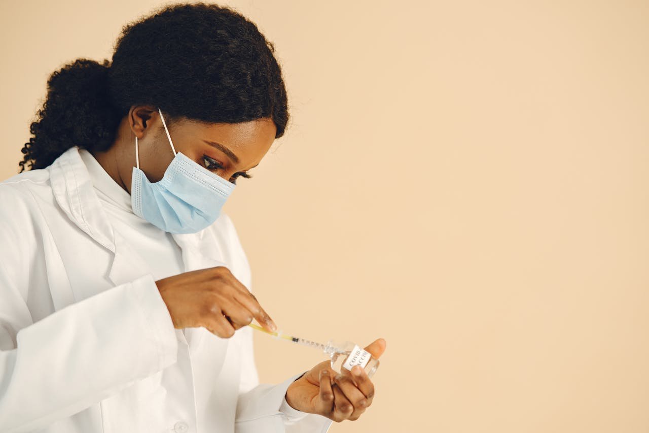 A female healthcare professional wearing a mask, preparing a vaccine syringe in an indoor setting.